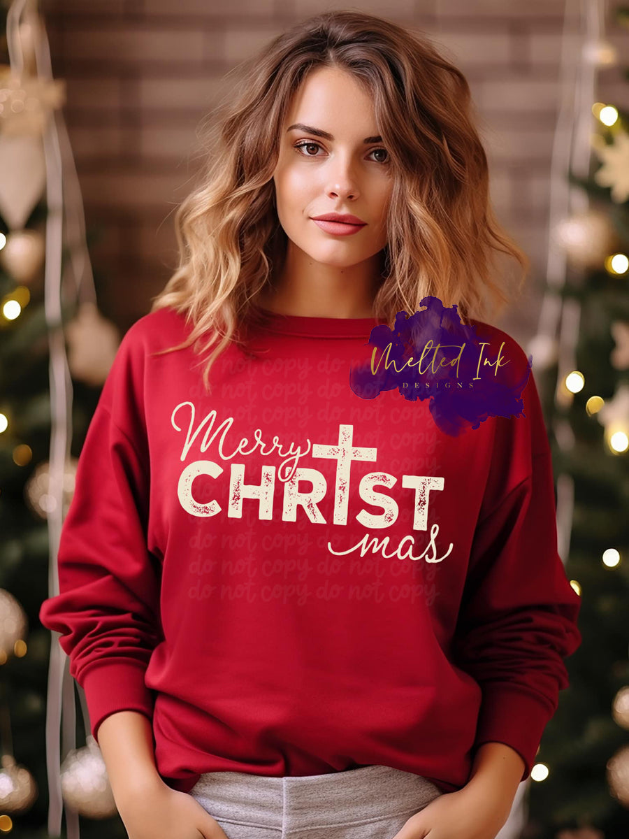 Photo is a mock up of design and is on a red sweatshirt. Design is beige color and says Merry ChrTstmas (The I in Christmas is a cross)