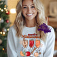 Design is a mock of and is on a white sweatshirt. Design is colored with red and orange color and says Merry Mimosas. Has a picture of 3 wine flutes with drinks in them and some christmas ornaments. 