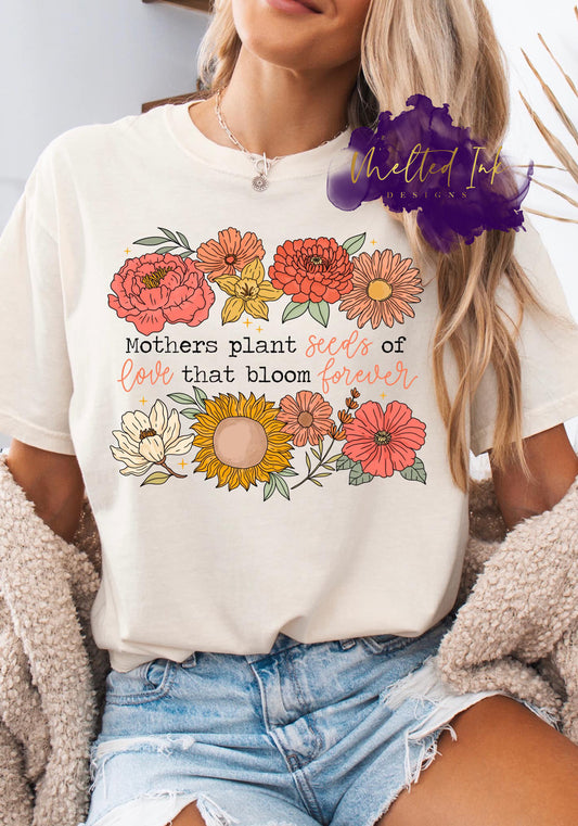 Shirt design with floral illustrations including sunflowers and zinnias, surrounding the phrase “Mothers plant seeds of love that bloom forever.” A meaningful floral design perfect for shirts, sweatshirts, and hoodies, ideal for Mother’s Day gifts.