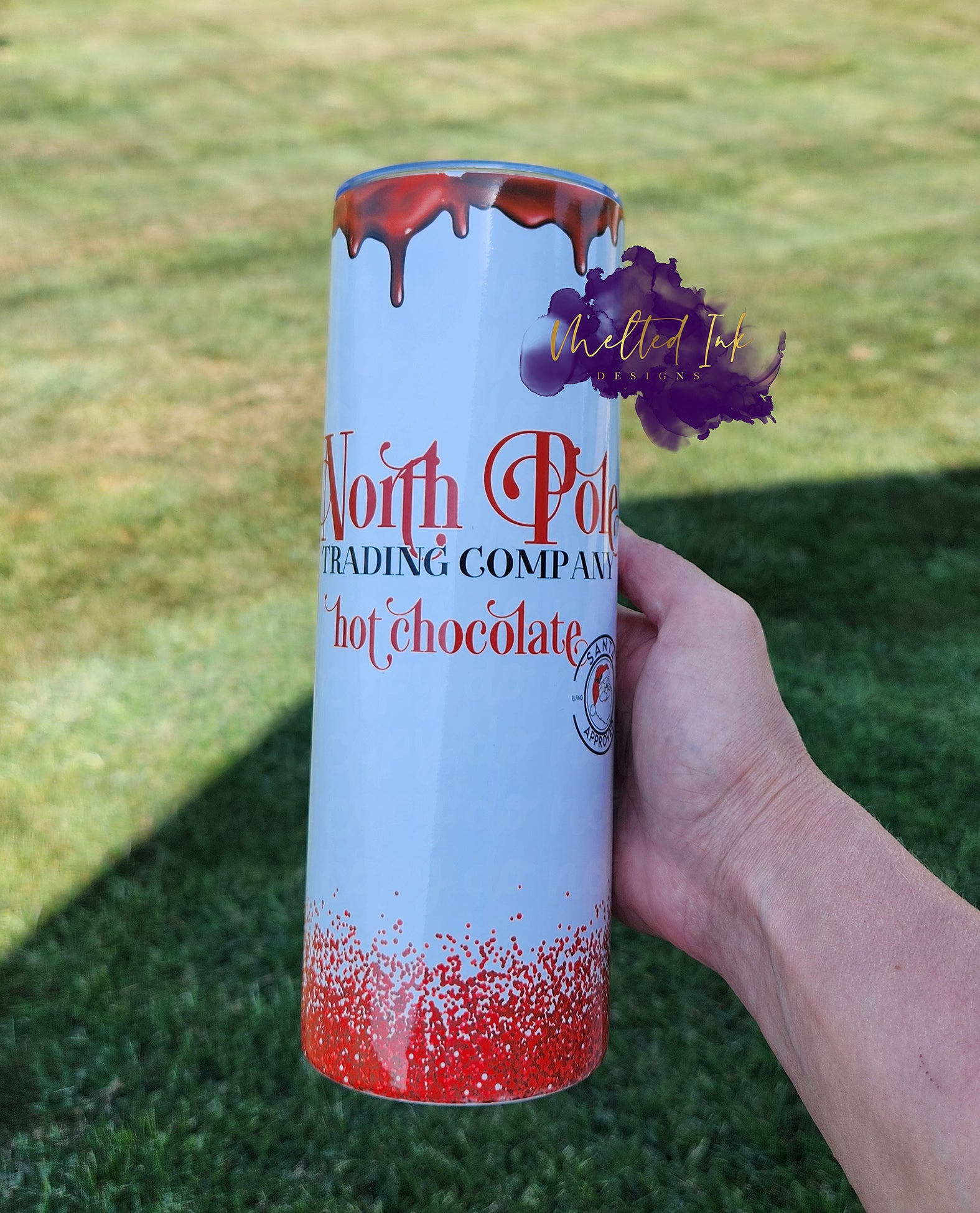 Photo consists of a 20oz tumbler that has melting chocolate at the top and faux red glitter at the bottom. Tumbler says North Pole trading company hot chocolate. 