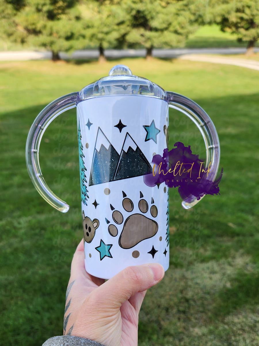 Photo is a picture of a childs sippy cup which also converts into a tumbler The design on the cup consists of mountains, bear paw, trees and bears. 