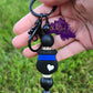 Photo consists of black beaded keychain bar that has a thin blue line badge with a white heart on it. It is accented with black silicone beads and rhinestone spacers on top and bottom of the badge. 