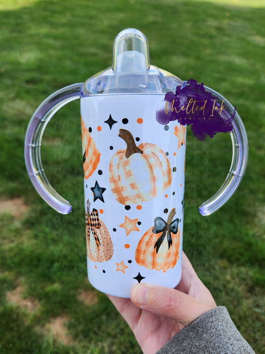 Photo consists of a kids sippy cup that converts into a tumbler. The design on the cup consists of plaid and polka dot orange pumpkins with stars and polka dots in the background. 