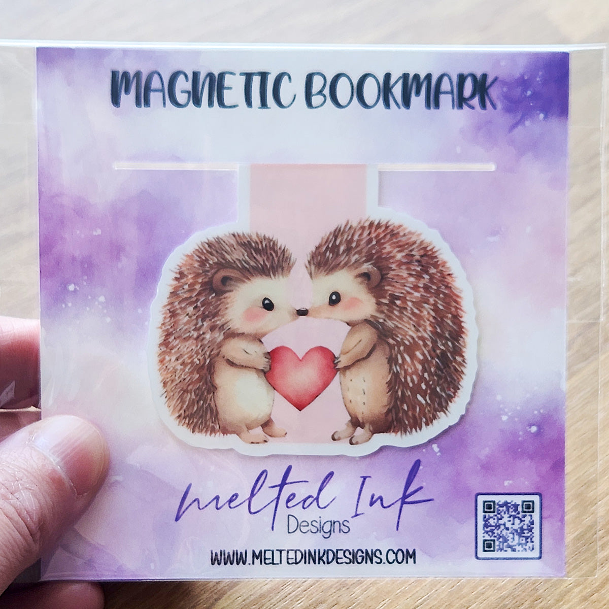 This magnetic bookmark features a sweet illustration of two adorable porcupines in love, holding a reddish-pink heart between them. 