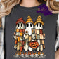 Image shows three cartoon-style ghosts wearing patchwork quilted robes, fall beanies, and sneakers. One ghost holds a pumpkin candy bucket. The design features warm autumn tones of orange, mustard, green, and cream — blending cozy fall and Halloween themes.