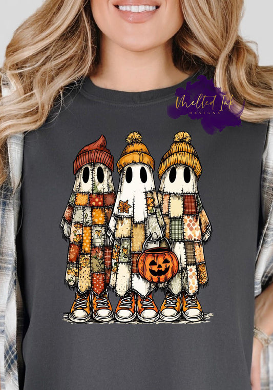 Image shows three cartoon-style ghosts wearing patchwork quilted robes, fall beanies, and sneakers. One ghost holds a pumpkin candy bucket. The design features warm autumn tones of orange, mustard, green, and cream — blending cozy fall and Halloween themes.