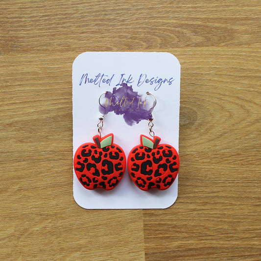 Photo is a picture of a pair of red apples that are leopard print earrings. 