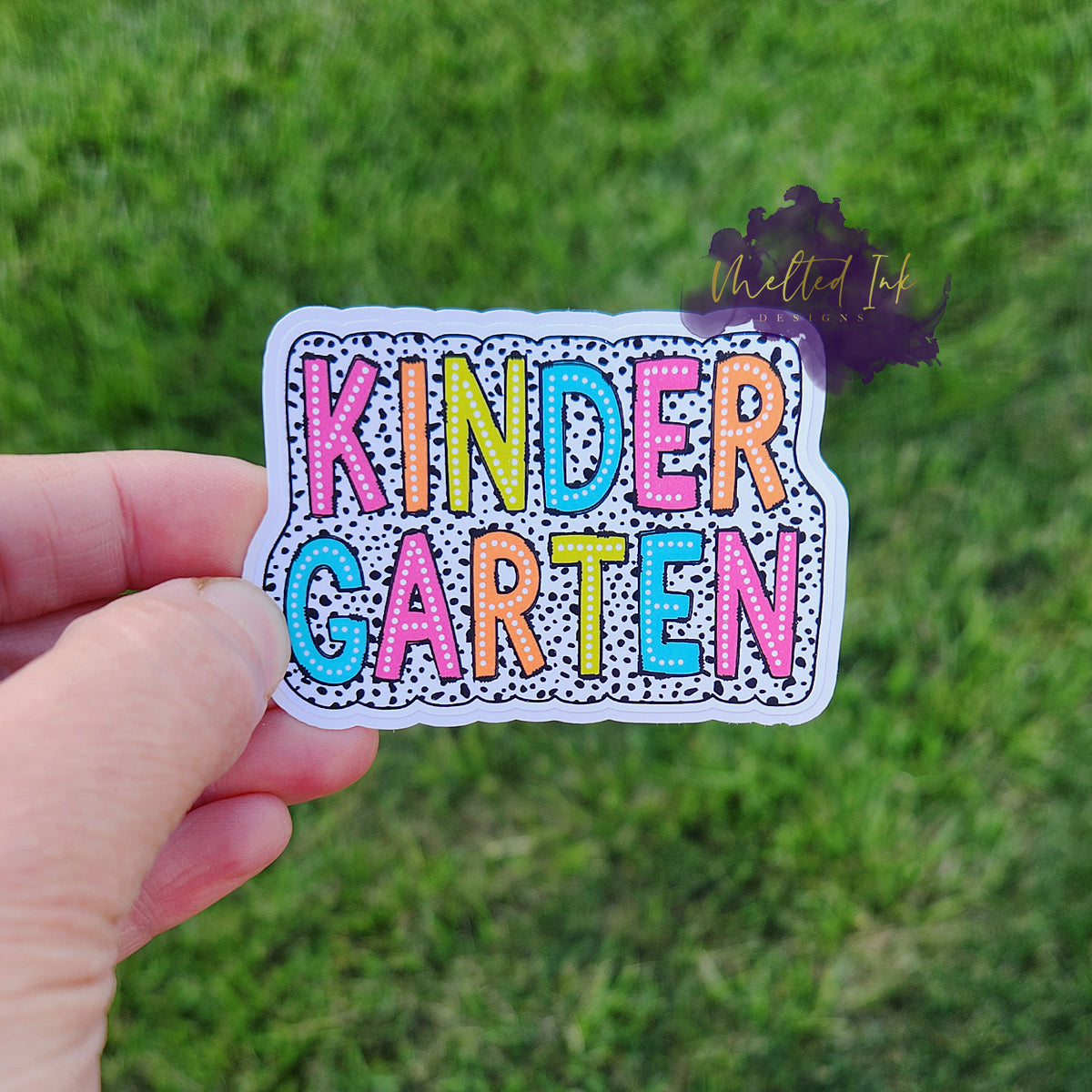 Photo is of a sticker that says kindergarten and has a black polka dot outline around it. 