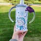 Photo consists of a kids sippy cup that converts into a tumbler. The design on the cup consists of snowmen faces wearing light blue santa hat and scarf and snowflakes