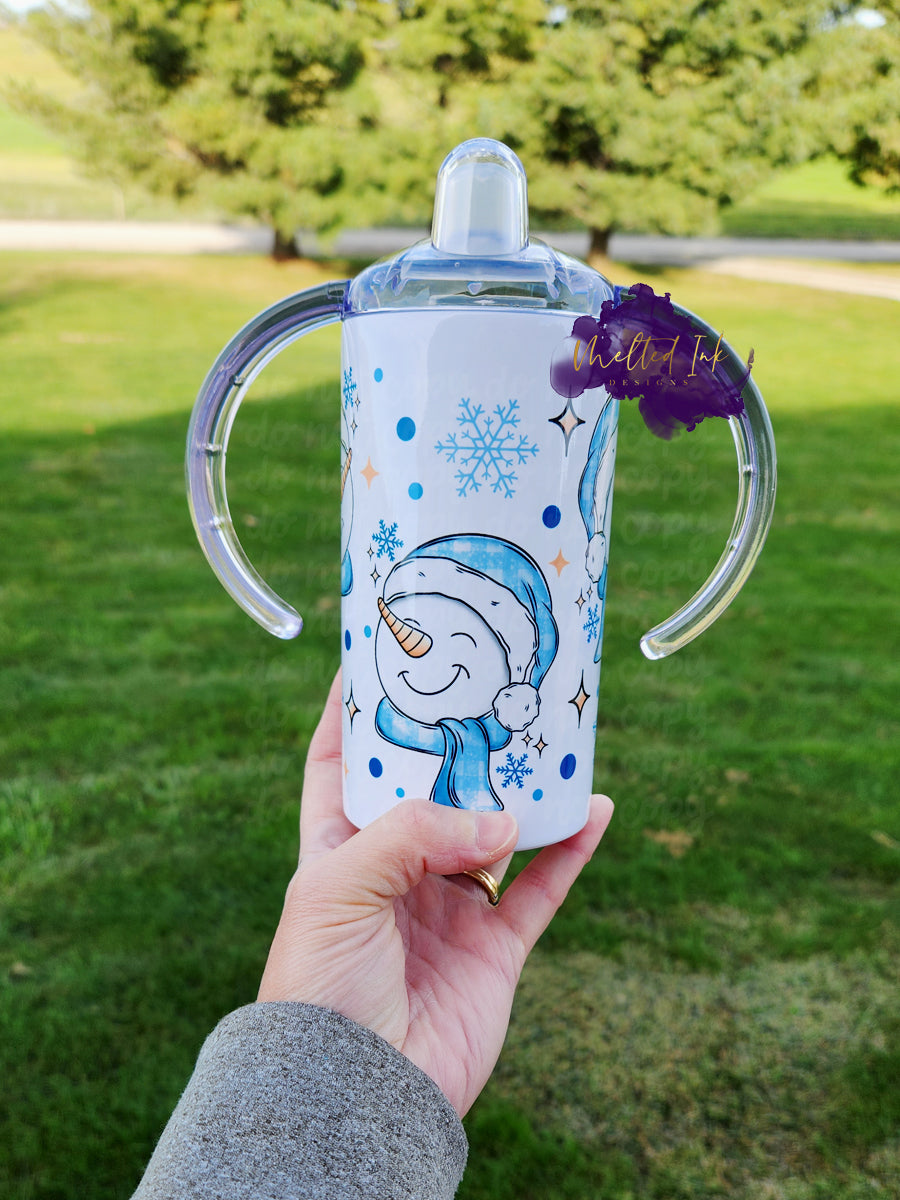 Photo consists of a kids sippy cup that converts into a tumbler. The design on the cup consists of snowmen faces wearing light blue santa hat and scarf and snowflakes