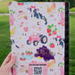 Farm-themed composition notebook featuring cows with bows, chickens, strawberries, flowers, pink rain boots, hay bales, and a vintage tractor on a light pink background with a customizable label area.