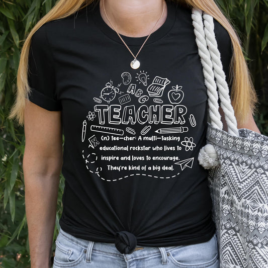 Photo is a mock up of the design. Print is white and pressed on black shirt. Design says Teacher and defines a teacher as a multi-tasking educational rockstar who lives to inspire and loves to encourage. They're kind of a big deal. 