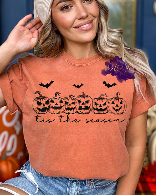 Photo is a mock up of the design. Print design is black and pressed on an orange shirt. Design consists of 6 smaller pumpkins in a row with 3 bats flying above them. Shirt says Tis the Season. 