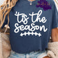 Shirt design with the phrase ’Tis the season” in playful script with a football stitch graphic below the text. A sporty fall football-themed design for shirts, sweatshirts, and hoodies.