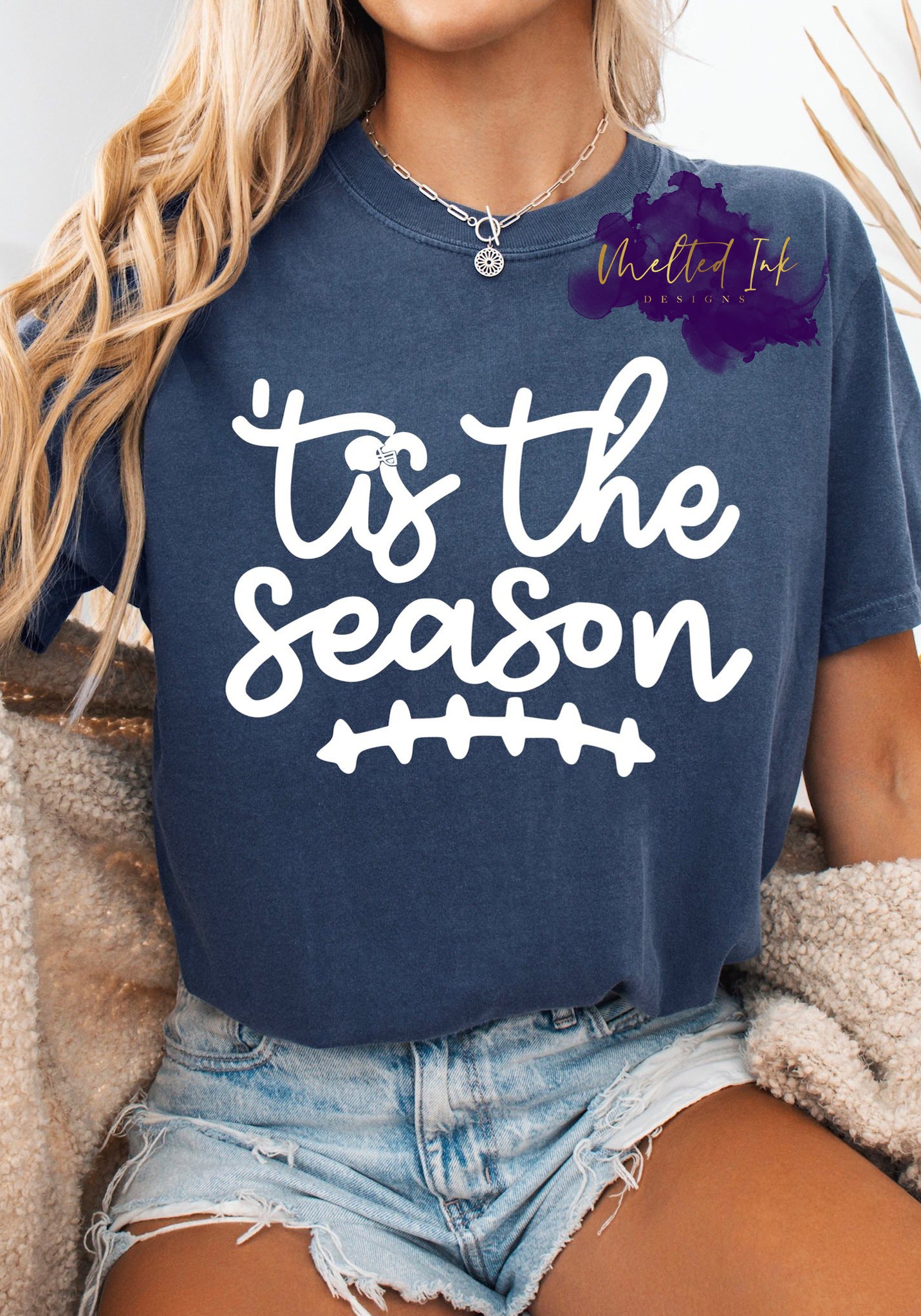 Shirt design with the phrase ’Tis the season” in playful script with a football stitch graphic below the text. A sporty fall football-themed design for shirts, sweatshirts, and hoodies.