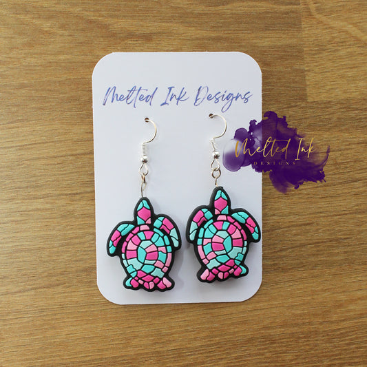 Photo is a picture of a pair of pink and aqua colored turtle earrings. 