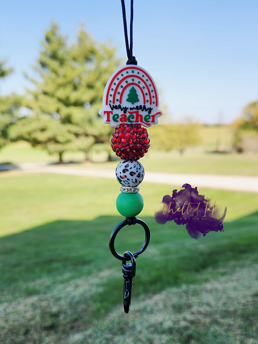 This Christmas-themed teacher lanyard features a focal bead that reads "Very Merry Teacher" in festive red and green colors. It includes a combination of a stylish red acrylic bead, a fun red and green leopard print silicone bead, and a solid green silicone bead, all contributing to a cheerful and vibrant design. The lanyard also comes with a keyring