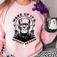Photo is a mock up of the design. Shirt design color is black and pressed on a pink sweatshirt. Design says: Wake Up It's Spooky Season with picture of Frankenstein. 