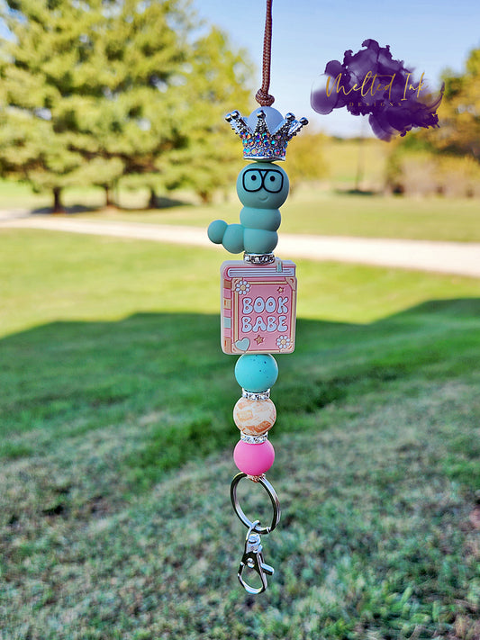 This charming lanyard features a whimsical worm focal wearing a rhinestone crown, sitting atop a focal bead shaped like a book that says "Book Babe." The design is accented with colorful silicone beads and small spacers, adding a fun and playful touch. It also includes a keyring .